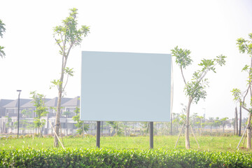 White blank advertising signboard in a green field with trees and houses on background 