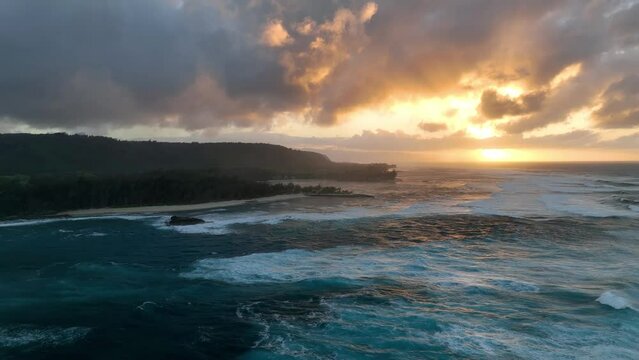 Aerial drone video captures the enchanting golden hour sunset in Hawaii, with big waves in the ocean.
