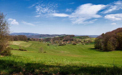 Fototapeta na wymiar Rolling hills with green grass, trees, and buildings on a spring day in Germany near Hinkelstein.