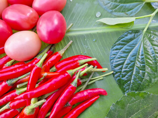 Picture of tomatoes and chili peppers placed on banana leaves.