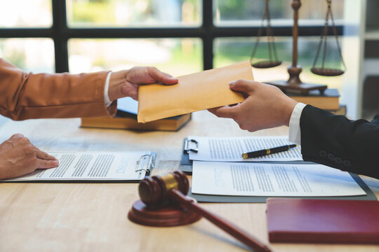 The hand of a corrupt businesswoman or politician is offering a bribe to a lawyer in the form of a brown money envelope for illegal business. Concept of corruption and bribery.