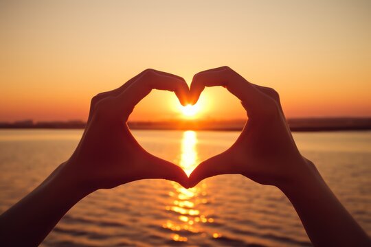 Hands in shape of love heart with sunset background