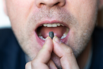 people eating roasted sunflower seed bite at crisp shell to eat seed inside. Black seed in men's teeth close-up. open mouth is gnawing on the seeds. - obrazy, fototapety, plakaty