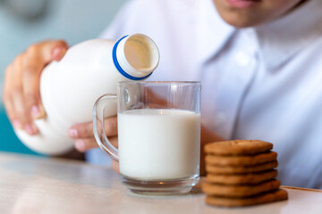 child girl pours milk into a glass from a bottle, cookies are on the table. Children's breakfast.