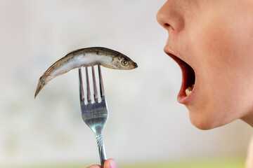 sprat in the hands, salty and fresh on white background. open mouth is eating fish. - obrazy, fototapety, plakaty