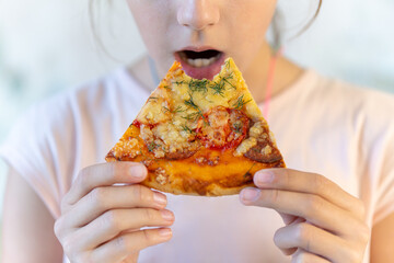 Teenage girl eats pizza. A girl holds a pizza in his hands and eats at a sidewalk cafe. Street food and fast food concept. Unhealthy diet as a cause of gastritis diseases.