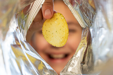 A teenage girl looks with joy at an open pack of chips. Appealing young lady opening mouth and...