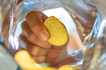 Child's hand taking chips junk food from opened packaging, Friend sharing food, unhealthy nutrition. inside pack view