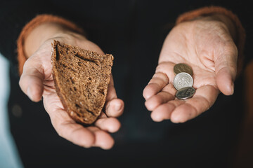 Hungry woman holding money and bread on a black background, hands with food close-up. Cash in the...