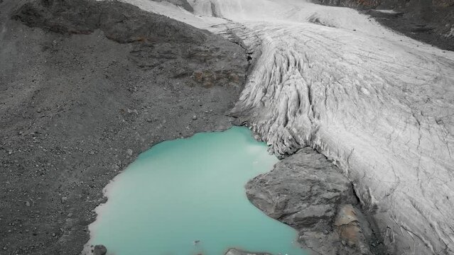 Aerialf flyover over Hohlaub glacier near Saas-Fee in Valais, Switzerland with a panu up view from the turquoise water of the glacial lake up to the crevasses in the ice and glowing mountain peaks.