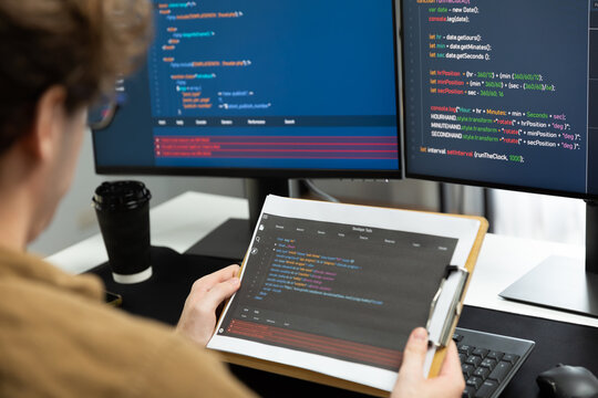 Working IT developer reading coding on document paper software with screens pc at modern office on coding application screens, creating updated program firmware information version concept. Gusher.