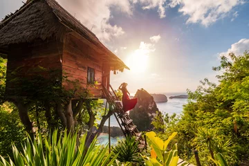 Rolgordijnen Young woman traveler enjoying and looking beautiful sunrise at the tree house in Nusa Penida island Bali, Indonesia © Kittiphan