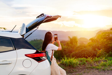 Young woman traveler sitting with car watching a beautiful sunrise over the mountain while...