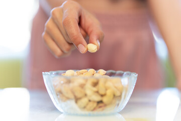 pistachios nuts in dish. Illuminated by natural light. A woman's hand takes a pistachio from a plate.