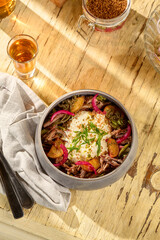 Overhead shot of a salad with roasted potatoes, pulled beef, and onions, served with smoked sour cream