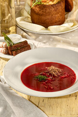 Traditional borscht served with rye croutons, sliced pork belly, and sour cream in bright sunlight