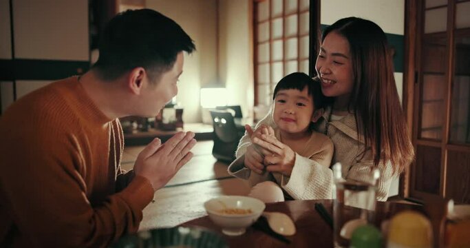 Japanese parents, girl child and dinner with bow, smile and teaching gratitude with noodles, night and nutrition in home. Kid, mother and dad for food, diet and dining room at family house in Tokyo