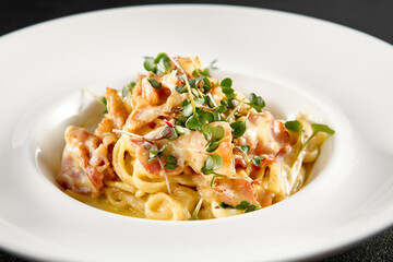 Classic carbonara pasta with a creamy sauce and garnished with fresh herbs, presented on a white plate