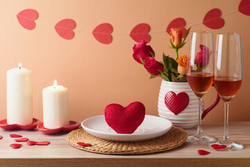 Valentine's day romantic dinner concept. Wooden table with plate, heart shape, wine, flowers and candles over peach color background