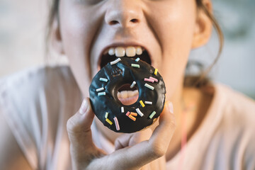 A sweet doughnut in hand. Little girl eating cupcake messily. The girl is eating sweet pastries. an open mouth and a chocolate donut. - obrazy, fototapety, plakaty