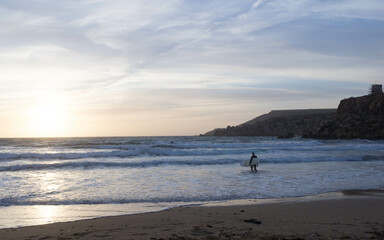 Fototapeta na wymiar Surfer on the seashore on the beach in Melieha. Sunset in Golden Bay Malta.