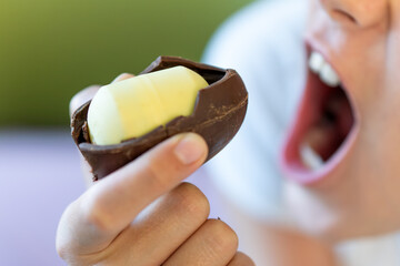 baby girl bites a chocolate egg with a plastic toy inside. harmful dangerous food for children