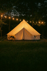 Night and warm light exposure of an illuminated bell tent surrounded by trees and a small camp fire...