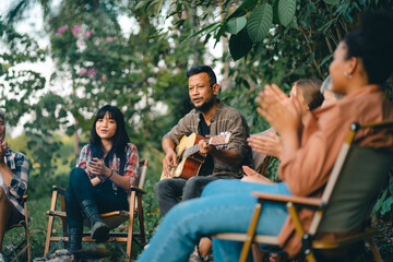 Group of man and woman friends and family singing and playing guitar during having breakfast together. People enjoy and fun outdoor lifestyle travel nature camping on summer holiday vacation.