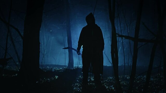 A lonely and frightening figure of a witcher in a dark forest at night. A man in a dark robe with a hood, a creature from the other world.
