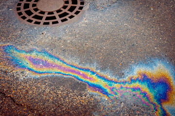 Oil slick on the asphalt road background drains into the storm drain.