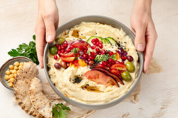 Hummus. Large bowl of homemade hummus garnished with chickpeas, vegetables and olive oil. Middle...