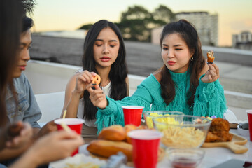 Young male and female friends enjoying dinner party at rooftop in evening