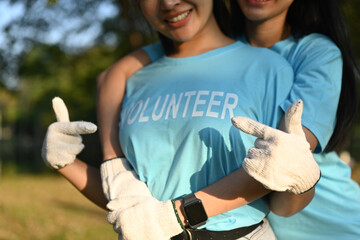 Cropped shot of two smiling young women volunteers pointing fingers at lettering on blue t-shirts