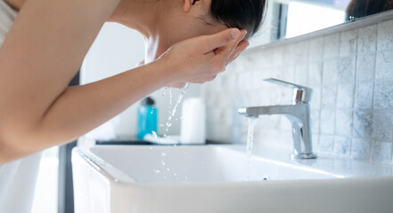 Asian woman washing her face with cold water at bathroom sink. Wash your face once in the morning...