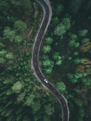 Fotobehang Bospad Aerial view taken by drone of a car driving on a forest road in autumn  © yalcinsonat