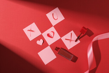 Valentine's day decoration with paper art cut. A lipstick unlabeled with lipstick streaks shaped like X and O like a checkerboard game on a red background with stage lighting.