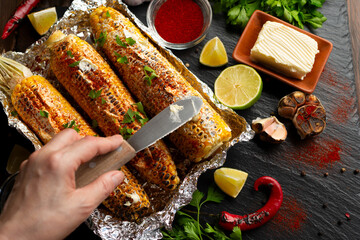 Grilled Sweetcorn with smoked paprika lime and butter on kitchen table being seasoned with table...