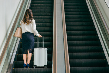 駅でエスカレーターに乗るスーツケースを持った出張・旅行帰りの女性・ビジネスウーマン
