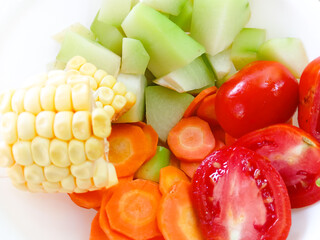pieces of chayote, carrots, tomatoes and corn in a white bowl. fresh vegetables to make healthy vegetable soup. cooking preparation. Close up