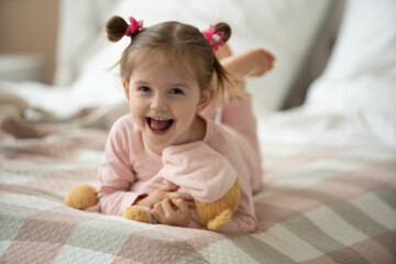 Cute little girl in pajama hugging her toy hare on the bed at home, happy childhood concept