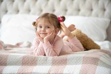 Cute little girl in pajama hugging her toy hare on the bed at home, happy childhood concept