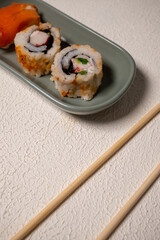 Chop sticks, mushrooms, noodle ramen, California rolls and Philadelphia rolls on a small plate on a pink background
