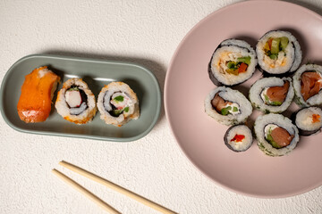 Chop sticks, mushrooms, noodle ramen, California rolls and Philadelphia rolls on a small plate on a pink background
