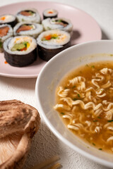 Chop sticks, mushrooms, noodle ramen, California rolls and Philadelphia rolls on a small plate on a pink background
