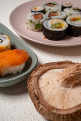 Chop sticks, mushrooms, noodle ramen, California rolls and Philadelphia rolls on a small plate on a pink background
