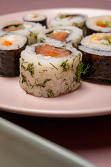 Chop sticks, mushrooms, noodle ramen, California rolls and Philadelphia rolls on a small plate on a pink background

