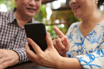 Cheerful senior couple resting at cafe table and shopping online via mobile app