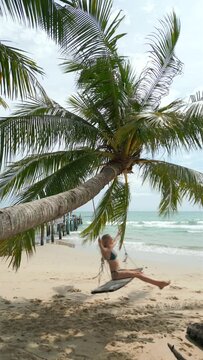 Young woman swinging on a swing on a beautiful palm tree on a tropical beach in Thailand.