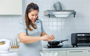 Millennial Asian professional female bakery pastry chef housewife holding cracking egg into glass bowl preparing whisking beating making flour dough baking delicious dessert in full decorated kitchen