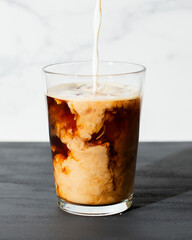 Stream of milk pouring into glass of iced coffee